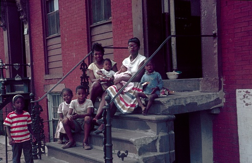 New York City, NY, USA, 1962. Two mothers with their children sitting on the stairs in front of their tenement.
