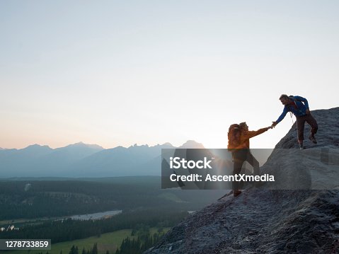 istock Two mountaineers offer helping hand on a rock ridge at sunrise above a valley 1278733859