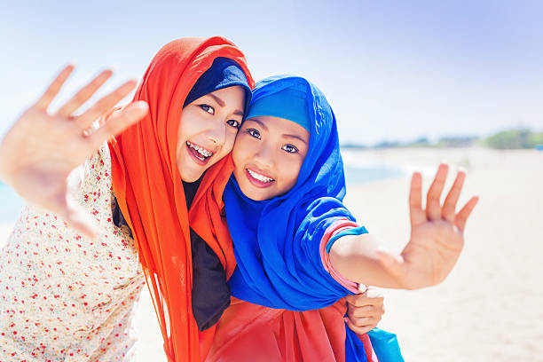 two muslim girls smiling at camera Mother and her daughter in headscarves standind on a beach indonesian girl stock pictures, royalty-free photos & images