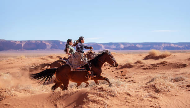 två infödda amerikanska indian systrar ridning hästar på sanddynerna i monument valley arizona - usa - desert cowgirl bildbanksfoton och bilder