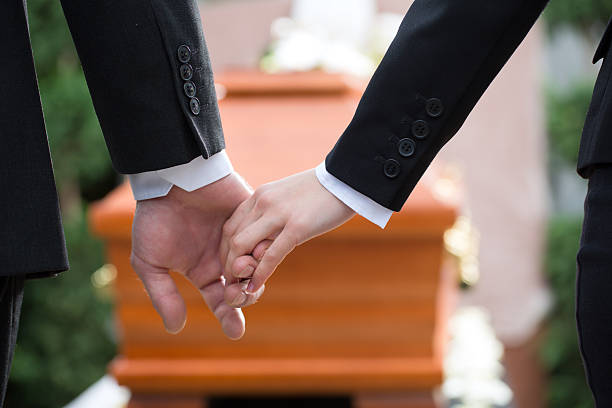 Two people holding hands at a funeral Religion, death and dolor - couple at funeral holding hands consoling each other in view of the loss undertaker stock pictures, royalty-free photos & images