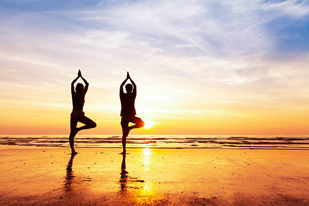 Two people practicing yoga tree position on the beach, sunset Two people practicing yoga tree position on the beach with beautiful sunset and reflection exotic asian girls stock pictures, royalty-free photos & images