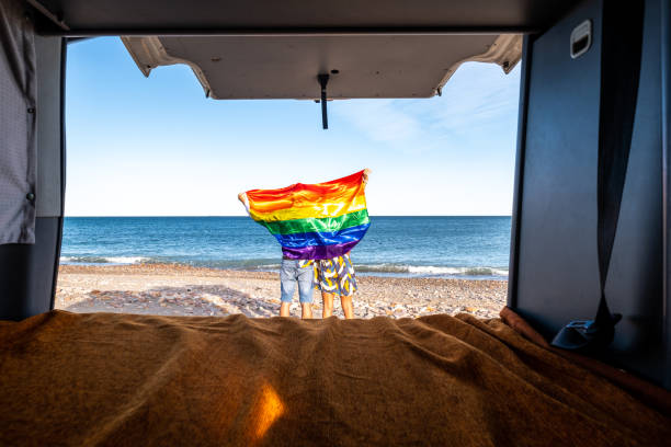 캠핑 밴 내부에서 서로 등을 가진 두 사람이 해변에서 lgtb 깃발로 덮여 있습니다. - progress pride flag 뉴스 사진 이미지
