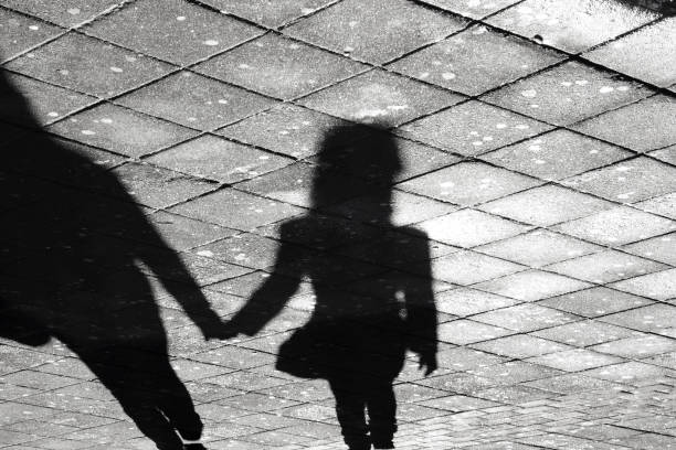 Two person holding hands shadow on a sidewalk Mother and daughter holding hands  shadow , on city street sidewalk in black and white approaching photos stock pictures, royalty-free photos & images
