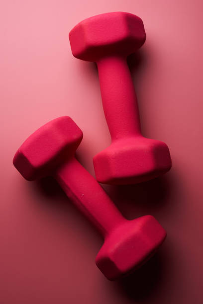Two pink female dumbbells isolated on pink background close-up with copy space. Fitness concept, weight loss and sport activity stock photo