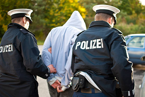 Two police officers are frogmarching a suspect Two police officers are frogmarching a criminal with a mask. german culture stock pictures, royalty-free photos & images