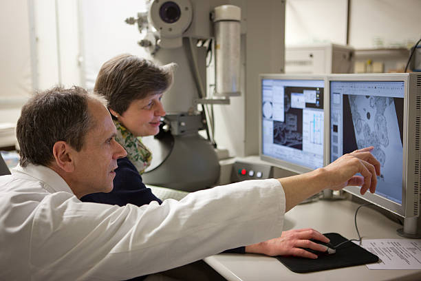 two researcher discuss results on monitor from an electronic microscope Medical Research: two scientist are analysing the results on monitor from an electronic microscope.  electron microscope stock pictures, royalty-free photos & images