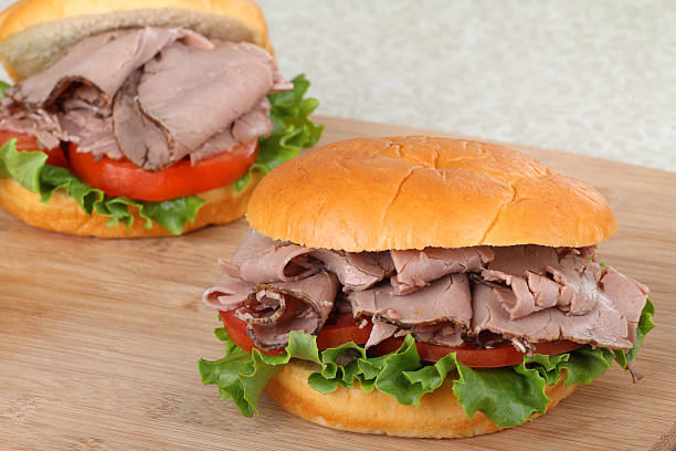 Two Roast Beef Sandwiches Two roast beef sandwiches with lettuce and tomato on a cutting board roast beef sandwich stock pictures, royalty-free photos & images