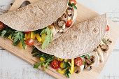 Two sandwiches with whole wheat wrap, chicken breast, mushroom and seasonal vegetables served on wooden board. Healthy and balanced meal
