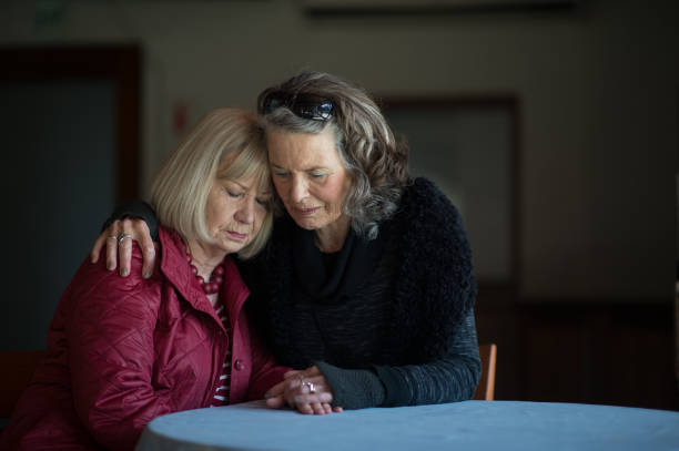 Two senior ladies supporting one another A senior lady supporting her friend after receiving sad bad news by holding hands comforting words and hugging her in support Stellenbosch Cape Town South Africa mourner stock pictures, royalty-free photos & images
