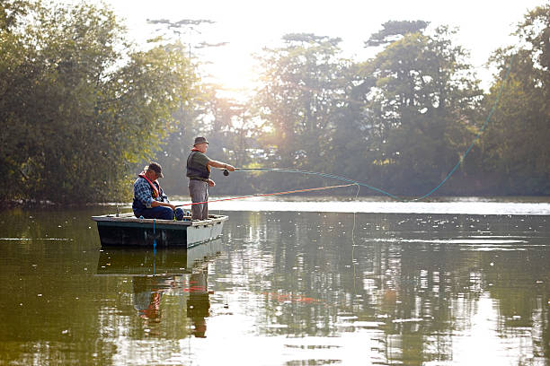 Two senior men in a boat fishing Two senior men in a boat fly fishing on a sunny day freshwater fishing stock pictures, royalty-free photos & images