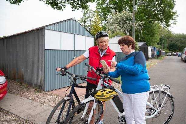 Two Senior Women Going Cycling Two caucasian senior women wearing sports clothing on a summers day. They are standing with their bicycles and cycling helmets, looking at directions on a smart phone. electric bike workout stock pictures, royalty-free photos & images