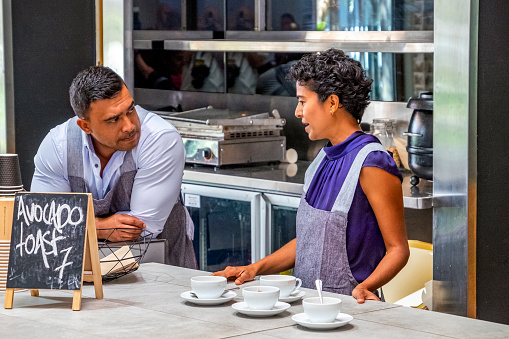 Two cafe owners/workers (small business) looking concerned in serious conversation: not serving customers, empty coffee/tea cups and saucers ready, 