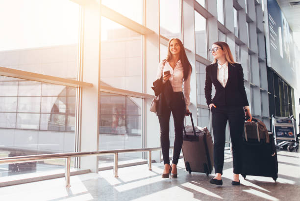 Two smiling business partners going on business trip carrying suitcases while walking through airport passageway Two smiling business partners going on business trip carrying suitcases while walking through airport passageway. tourist stock pictures, royalty-free photos & images
