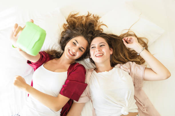 Two Smiling Females Lying on Bed and Taking Selfie Two Smiling Females Lying on Bed and Taking Selfie,indoor shot gay spooning stock pictures, royalty-free photos & images