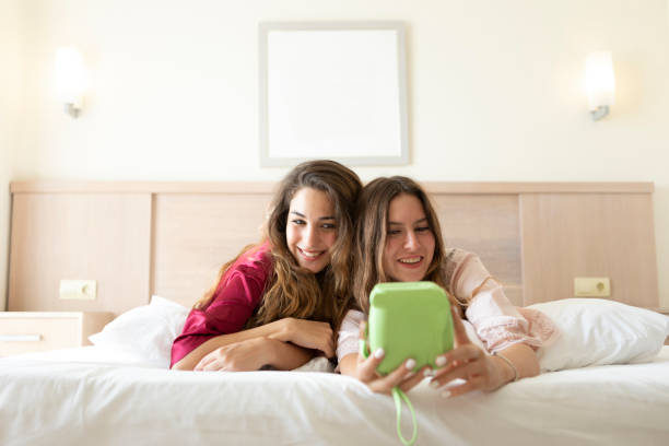 Two Smiling Females Lying on Bed and Taking Selfie Two Smiling Females Lying on Bed and Taking Selfie,indoor shot gay spooning stock pictures, royalty-free photos & images