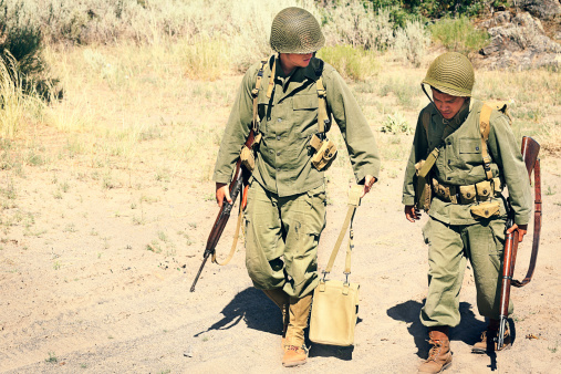 Two soldiers walking along a dusty road. Vintage, authentic army uniforms and weapons.
