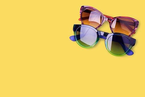 Two sunglasses on yellow background close up top view, fashionable eye sunshades, pair of trendy modern female and male eyeglasses, summer beach holidays concept, ultraviolet protection, copy space