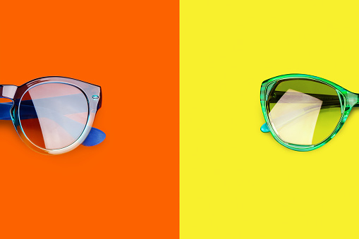 Two sunglasses yellow orange red background closeup top view, fashion man and woman sunshades, pair of trendy modern female and male eyeglasses, summer beach holidays uv protection concept, copy space
