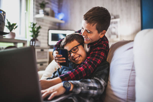 Two teenage boys with gadgets on couch at home stock photo
