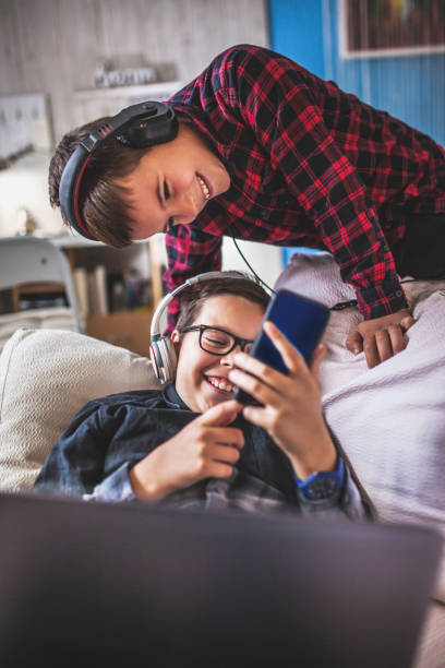 Two teenage boys with gadgets on couch at home stock photo