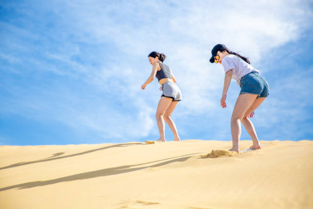 Two teenage girls are sandboarding down the sand dune together at Anna Bay Australia. stock photo