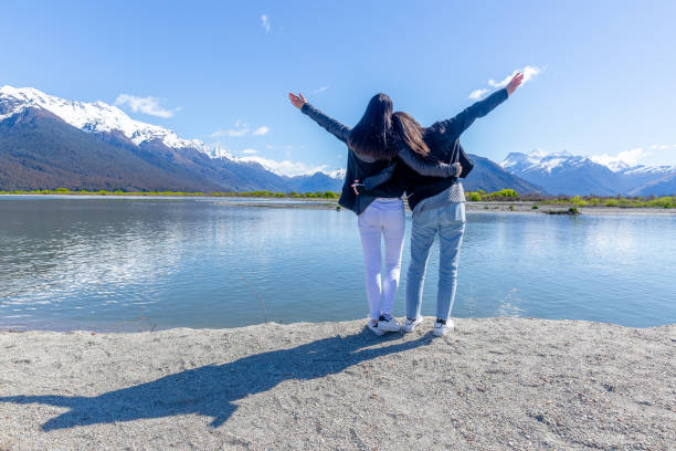 Two teenage girls embracing mountain and lake views with open arms. stock photo