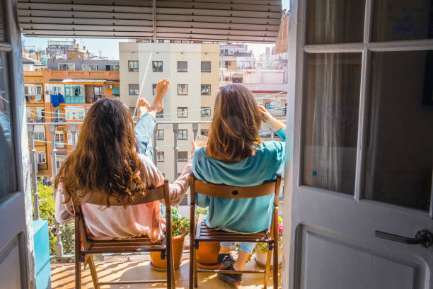Two teenage girls, sunbathing, sitting on chairs on the balcony , enjoying the cityscape stock photo