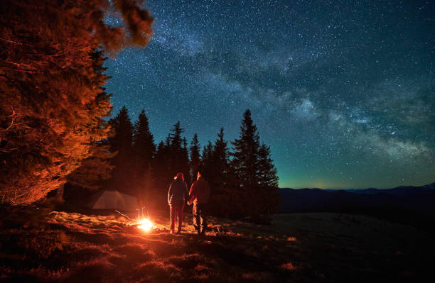 Two tourists resting by fire during night camping in mountains. stock photo