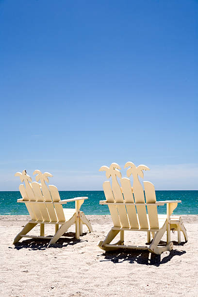 Two white wooden beach chairs on sand with ocean Two empty beach chairs overlooking a beautiful turquoise ocean.  naples florida beach stock pictures, royalty-free photos & images