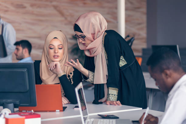 Two woman with hijab working on laptop in office. stock photo