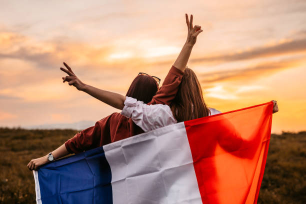 Two women  covering themselves with flag of France on meadow stock photo