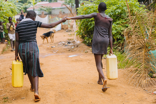 Two women holding hands while carrying water cans after fetching water from the public well in Entebbe, Uganda