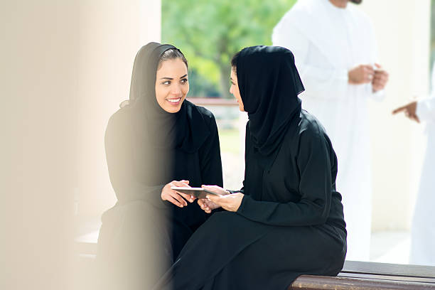Two women looking at a booklet Two middle eastern women dressed in abaya looking at digital tablet outdoors. abaya clothing stock pictures, royalty-free photos & images