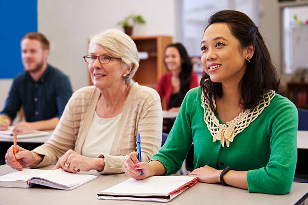 Two women sharing a desk at an adult education class Two women sharing a desk at an adult education class look up adult education stock pictures, royalty-free photos & images