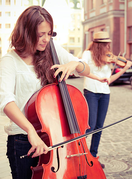 Two women strings duet playing violin and cello on street stock photo