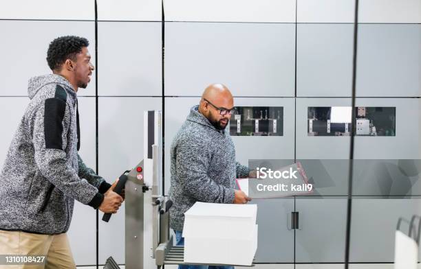 Two workers in printing plant, moving stack of paper