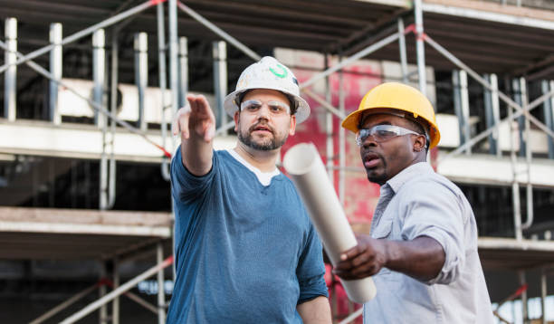 twee arbeiders praten op een bouwplaats, plattegronden - aanwijzen plattegrond stockfoto's en -beelden
