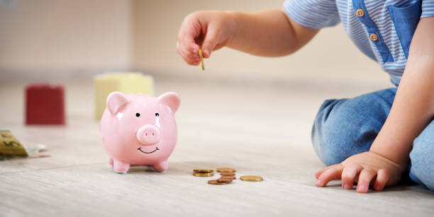 two years old child sitting on the floor and putting a coin into a piggybank two years old child sitting on the floor and putting a euro coin into a piggybank. allowance stock pictures, royalty-free photos & images