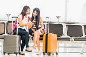 若いアジアの女の子を 2 つのスマート フォンを使用してフライトをチェックまたはウェブチェッ クイン、空港待機席に一緒に座る。空の旅をライフ スタイル、刺激的な夏休み旅行や携帯ガ�