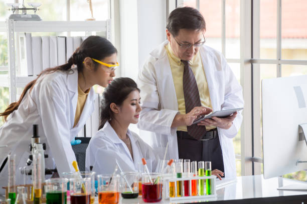 Two young  asian woman research scientist and senior man supervisor preparing test tube and analyzing microscope With Computer in  Laboratory . teamwork . three people stock photo