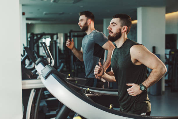 Two young man running on treadmill at gym stock photo