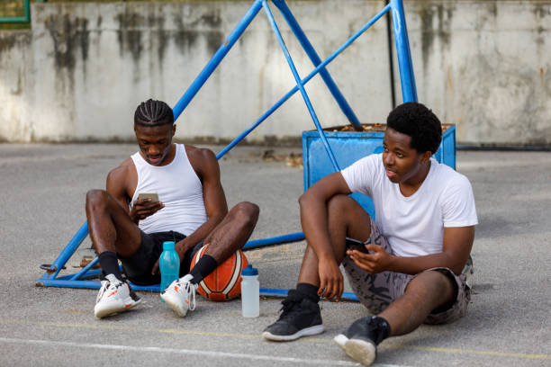Two Young Men Are Resting After Basketball Game And Use Smart Phones stock photo