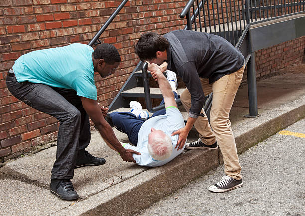 Two young men helping fallen down senior. Multi ethnic stock photo