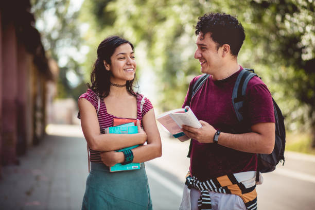 Two young students standing on street with books and talking. stock photo