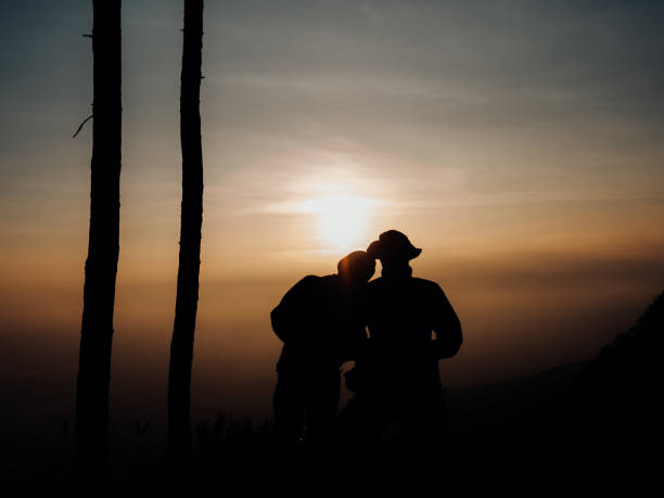 Two young tourists Silhouette, watching the sunrise at the edge of the cliff in the early morning. In the tourist season at Phu Kradueng National Park stock photo