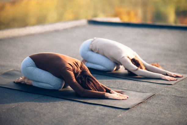 zwei junge frauen, die yoga asana kind pose auf dem dach im freien zu tun - yoga poses stock-fotos und bilder