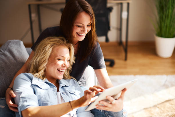 Two young women sitting on sofa use a digital tablet and laughing stock photo