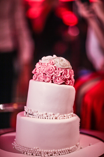 Two-tiered white wedding cake decorated with pink flowers.