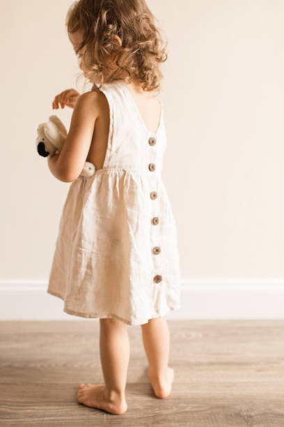 Two-Year-Old Toddler Girl Hugging & Kissing Her Little Dog Toy While Wearing a Cream-Colored Linen Dress & a Bow at Home During COVID-19 Two-Year-Old Toddler Girl Sitting on the Floor, Hugging Her Little Dog Toy While Wearing a Cream-Colored Linen Dress & a Bow at Home During COVID-19 beautiful young brunette girl playing with her dog stock pictures, royalty-free photos & images